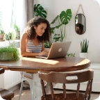 Young woman sits at dining room table and uses a laptop.